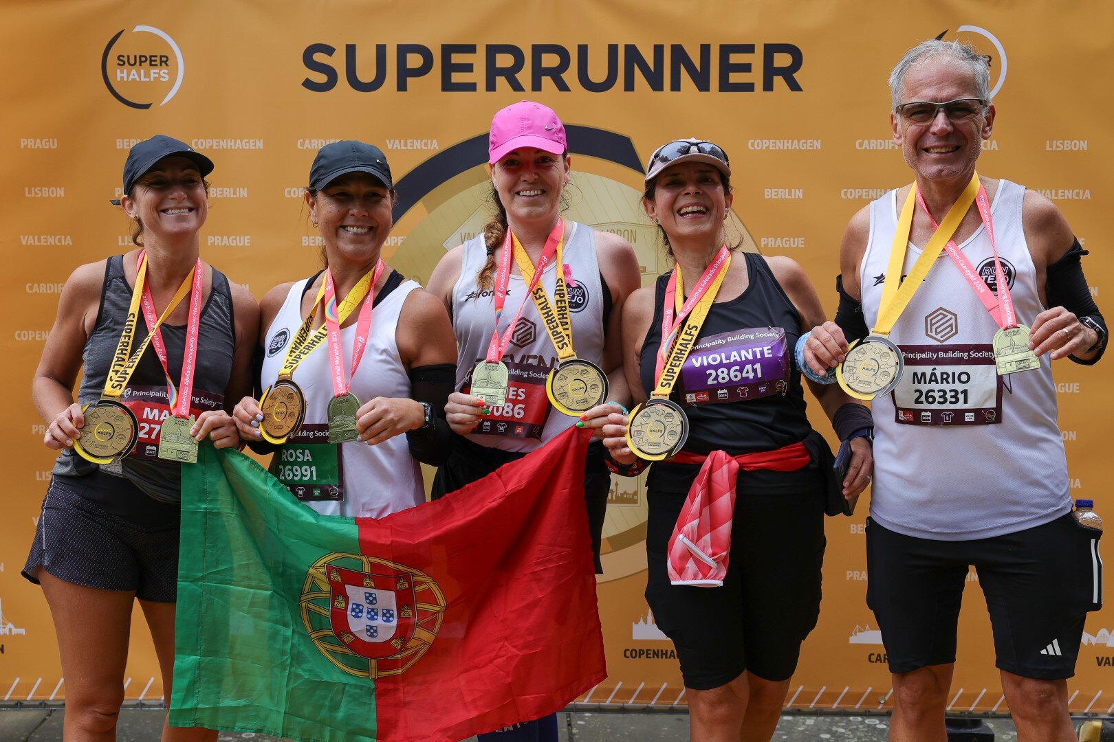 5 runners holding their medals lined up in front of a superrunner banner at one of the SuperHalfs half marathons.